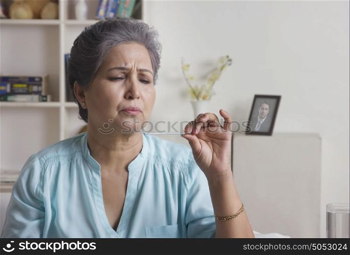 Old woman checking temperature on thermometer