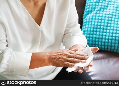 old woman cleaning her hands with white soft tissue paper at home