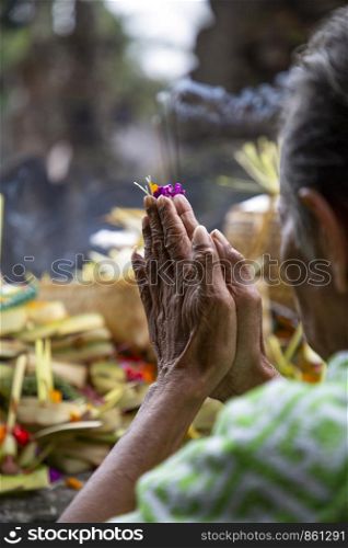 Old woman folds hands to prayer with prey in Hindu temple Bali