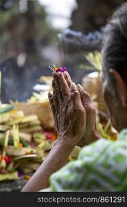 Old woman folds hands to prayer with prey in Hindu temple Bali