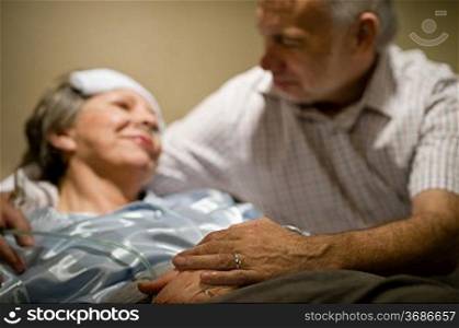 Old woman in pain lying bed holding hands with husband