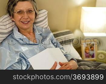 Old woman in pajamas lying in bed looking at camera