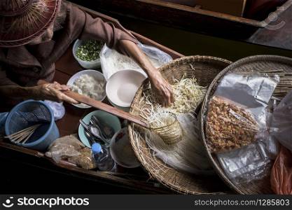 old woman making thai noodle food by sailing in local floating boat market