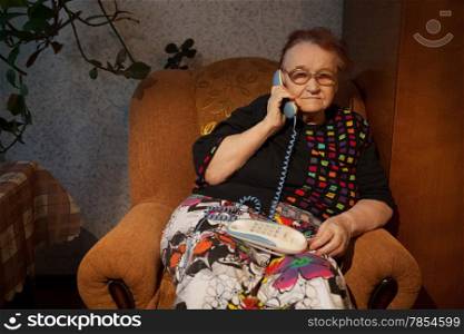 Old woman talking on the home phone sitting in the arm-chair in the evening