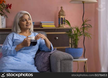 Old woman with holding a cup of tea in hand looking away and thinking