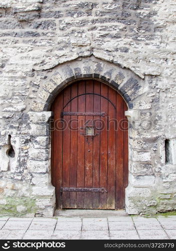 Old wooden arched door in stone wall.