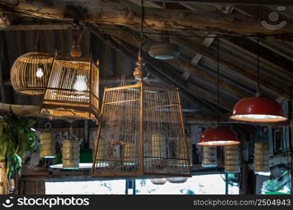 Old wooden birdcage hanging from a wooden beamed ceiling to decorate the interior of country-style pub or restaurant. Vintage birdcage, Antique birdcage, Selective focus.