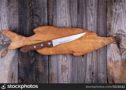 old wooden board in the form of a fish figure and a knife on a gray table, top view