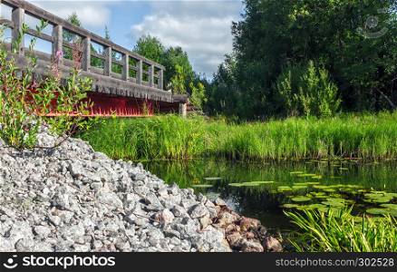 Old wooden bridge over the river in the green on a sunny day.. Wooden Bridge Over The River