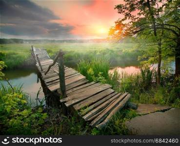 Old wooden bridge through narrow river at sunrise