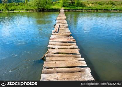 Old wooden bridge through the river with green trees on the banks