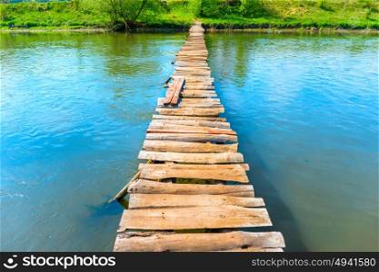 Old wooden bridge through the river with green trees on the banks