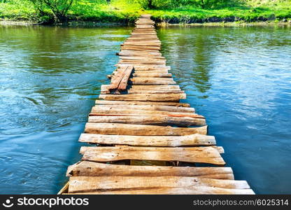 Old wooden bridge through the river with green trees on the banks