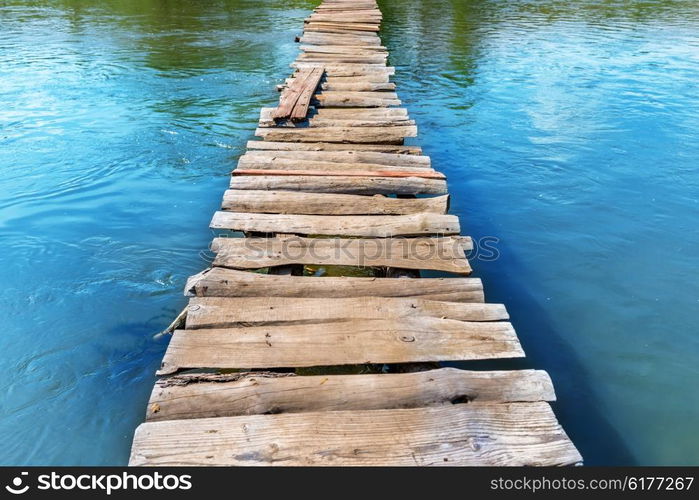 Old wooden bridge through the river with green trees on the banks