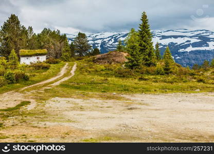 Old wooden cabin hytte with grass on the roof in norwegian green mountains. Beautiful landscape in Norway, Scandinavia. Old wooden cabin in forest Norway