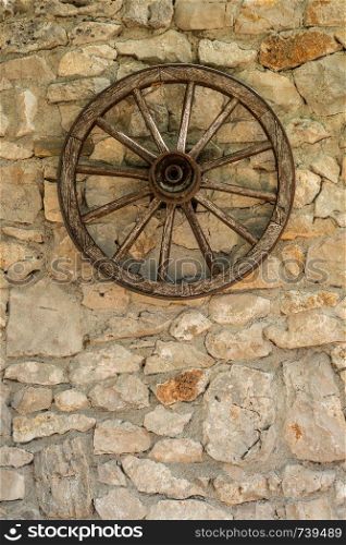Old wooden cart wheel on stone farmhouse wall. Cartwheel hanging on old rustic stone wall of farmhouse