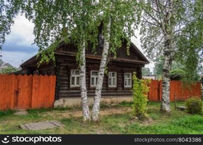 Old wooden country house with birches in front, summer day