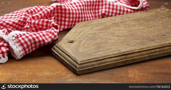 old wooden cutting board and folded red and white cotton kitchen napkin on a wooden brown background, top view