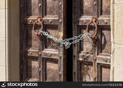 Old wooden door in Tuscany, Italy. Slightly ajar but locked with a modern chain