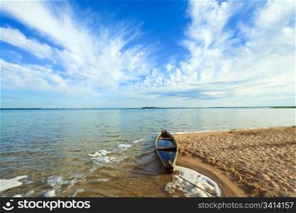 Old wooden fishing boat flooding near the lake shore and summer sky behind (Svityaz, Ukraine)