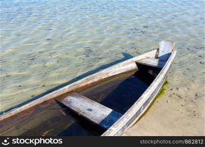 Old wooden fishing boat on summer lake bank.