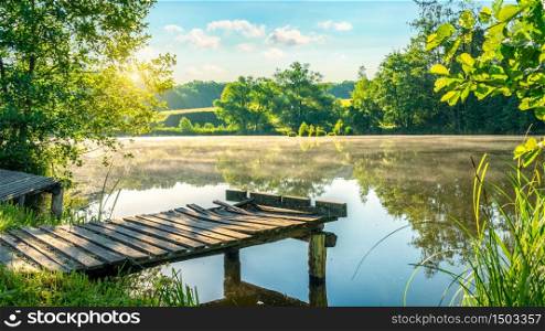 Old wooden fishing pier on river in foggy morning