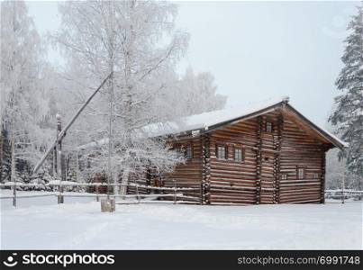 Old wooden house with shadoof in Northern Russian village. Open air museum Malye Korely near Arkhanglesk, Russia. Frosty winter day.