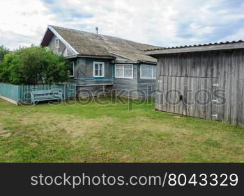 Old wooden house with shed and lawn in russian village, summer day