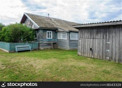 Old wooden house with shed and lawn in russian village, summer day