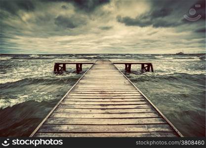 Old wooden jetty, pier, during storm on the sea. Dramatic sky with dark, heavy clouds. Vintage