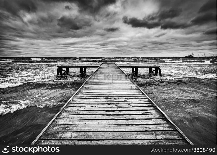 Old wooden jetty, pier, during storm on the sea. Dramatic sky with dark, heavy clouds. Black and white