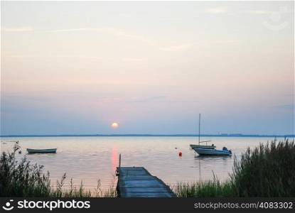 Old wooden jetty with anchored rowing boats at evening in a calm bay