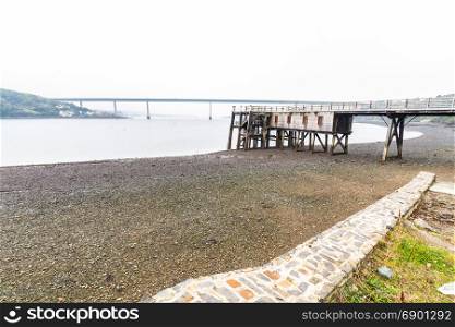 Old wooden jetty with the Cleddau Bridge in the background. Burton Ferry, Pembrokeshire, Wales, United Kingdom.