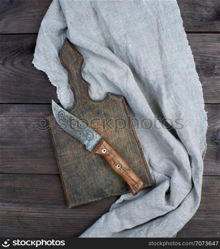 old wooden kitchen board and vintage knife on a brown wooden background, top view