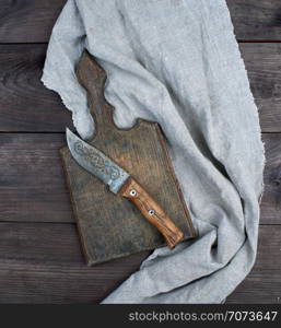 old wooden kitchen board and vintage knife on a brown wooden background, top view