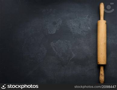 old wooden rolling pin for rolling dough on a black background, top view. Copy space