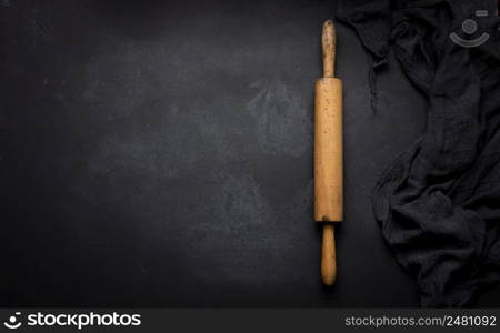 Old wooden rolling pin for rolling dough on a black background, top view. Copy space