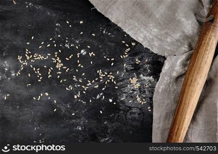 old wooden rolling pin on a black background, near a gray linen towel, top view, sprinkled with flour and wheat, copy space