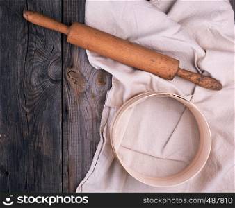 old wooden rolling pin on a textile napkin with embroidery and a round sieve for flour, gray wooden background