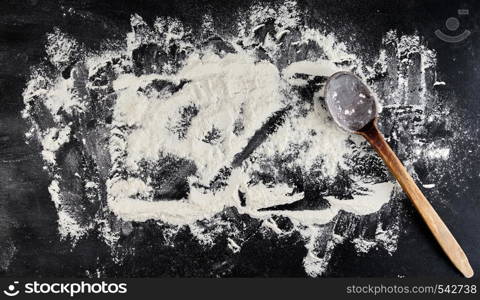 old wooden spoon and white wheat flour scattered on a black background, product is spread over the surface, kitchen background, top view