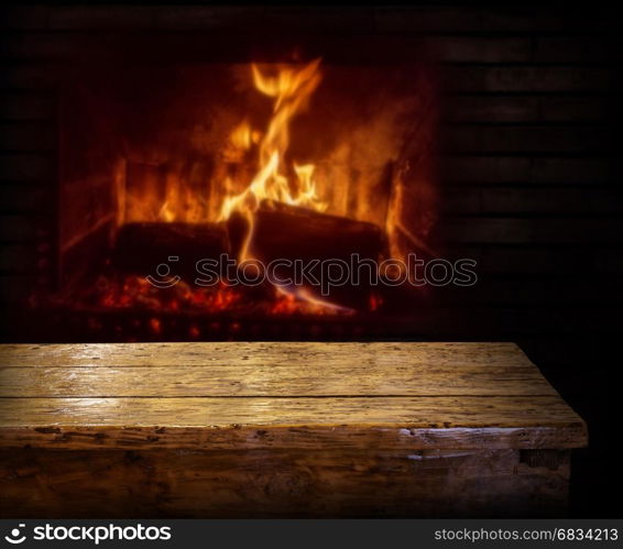 Old wooden table and fireplace with warm fire on the background.