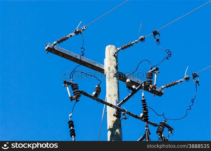 Old wooden telephone or electrical pole and metal bar with cables and insulators on right side, against clear blue sky.