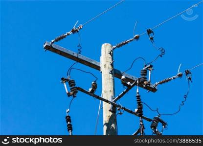 Old wooden telephone or electrical pole and metal bar with cables and insulators on right side, against clear blue sky.