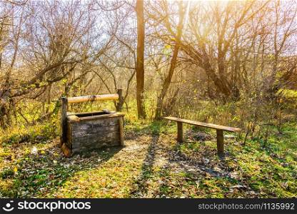 Old wooden well-draw and bench in autumn forest. Well-draw in forest