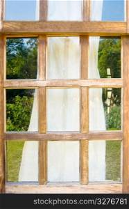 Old wooden windows with drape and reflect sky and grassland