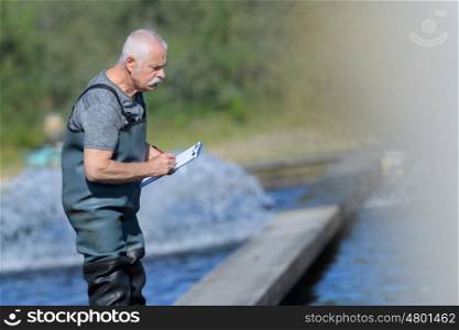 old worker at a fish farm writing down data