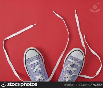 old worn sneakers with untied white laces on a red background, top view
