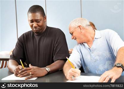 Older college student trying to copy off a younger student&rsquo;s test paper.