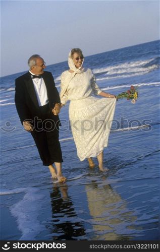 Older Couple Walking Along Ocean Beach In Formal Wear
