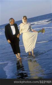 Older Couple Walking Along Ocean Beach In Formal Wear